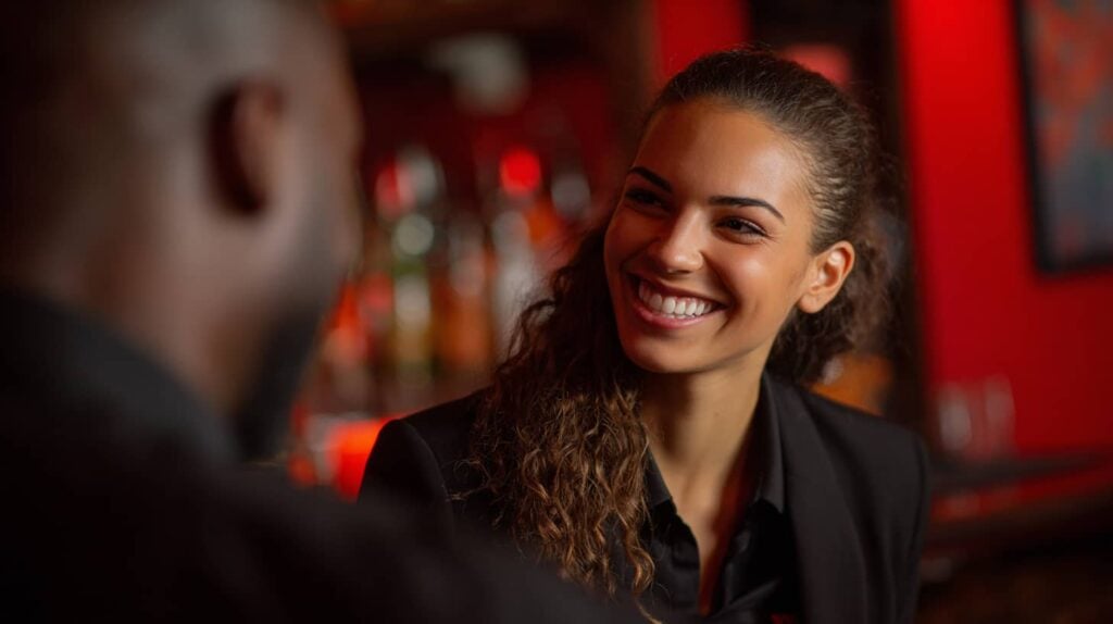 Frau lächelt am Bar, während sie über die Cocktailmaschine von The Cocktailmaker spricht, ideal für Gastronomie und Veranstaltungen.